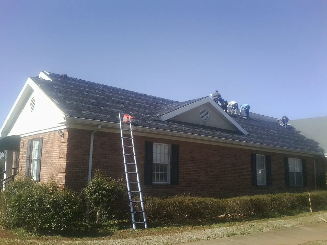 Crew tearing shingles off a brick ranch roof with a ladder set — Metal Roof Repair work by our crew in Grantville