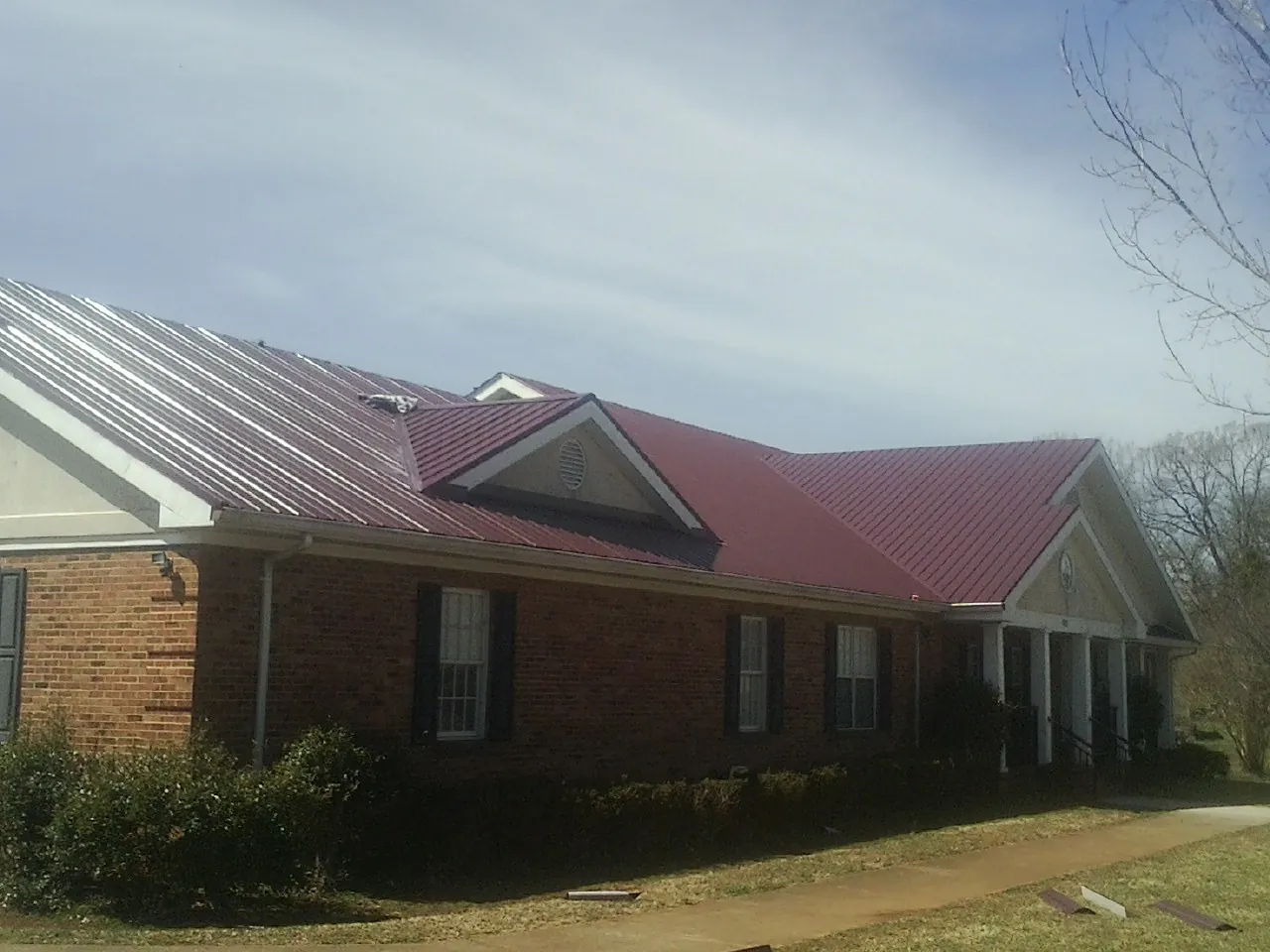 Red metal roof with gabled entries on a long brick building, from a Hail Damage Roof Repair job in Grantville