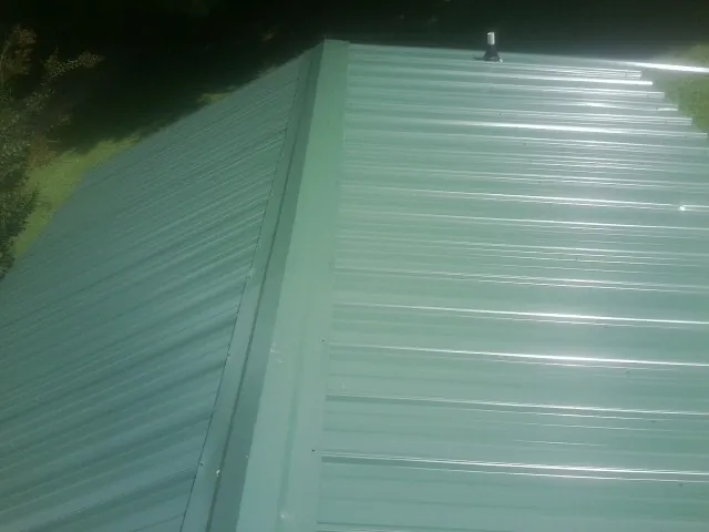 New green metal panels meeting at the ridge of a roof — Flat Roof Repair work by our crew in Grantville