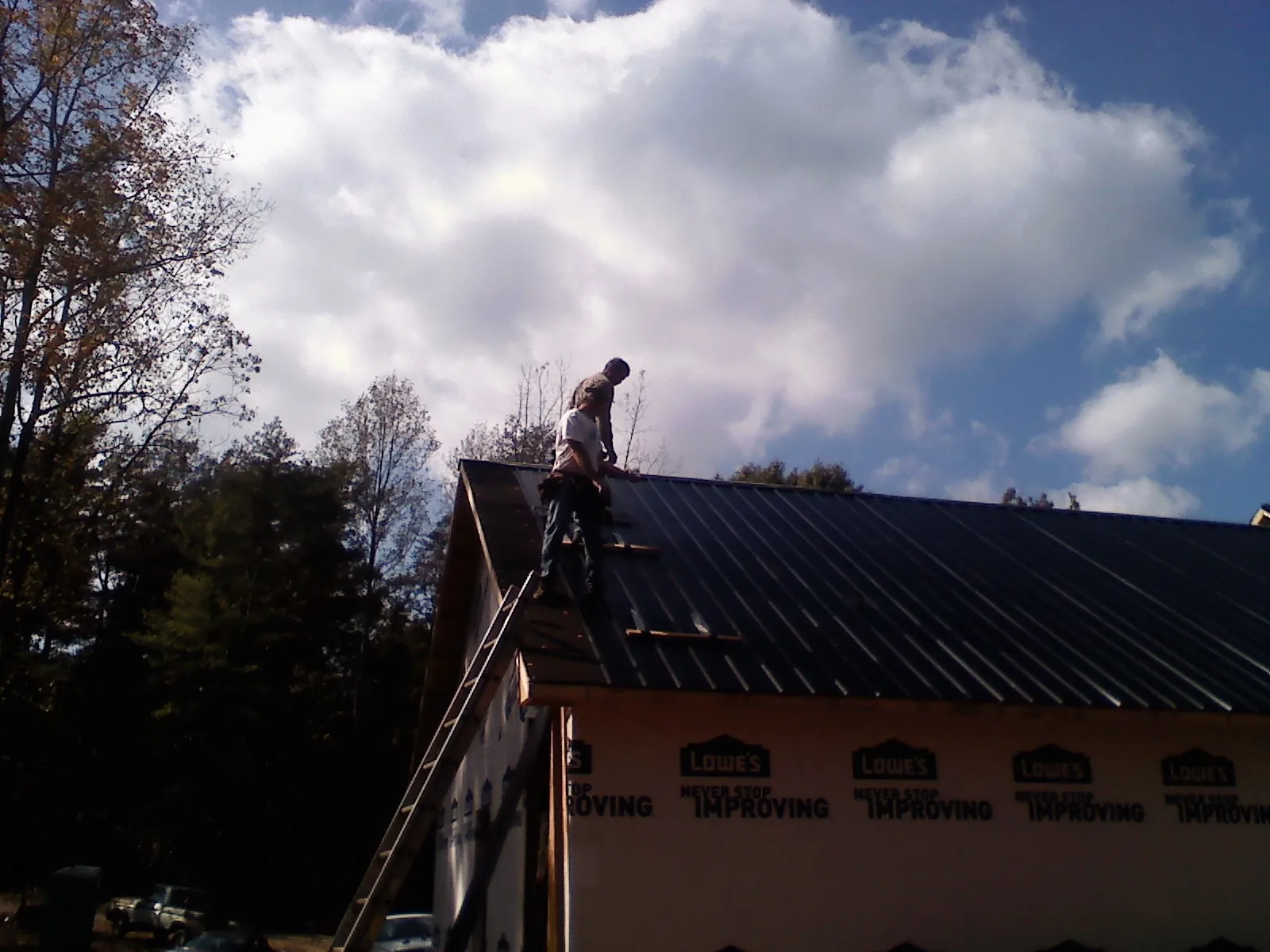 Roofer fastening dark metal panels high against a cloudy sky, from a Roof Inspection job in Grantville